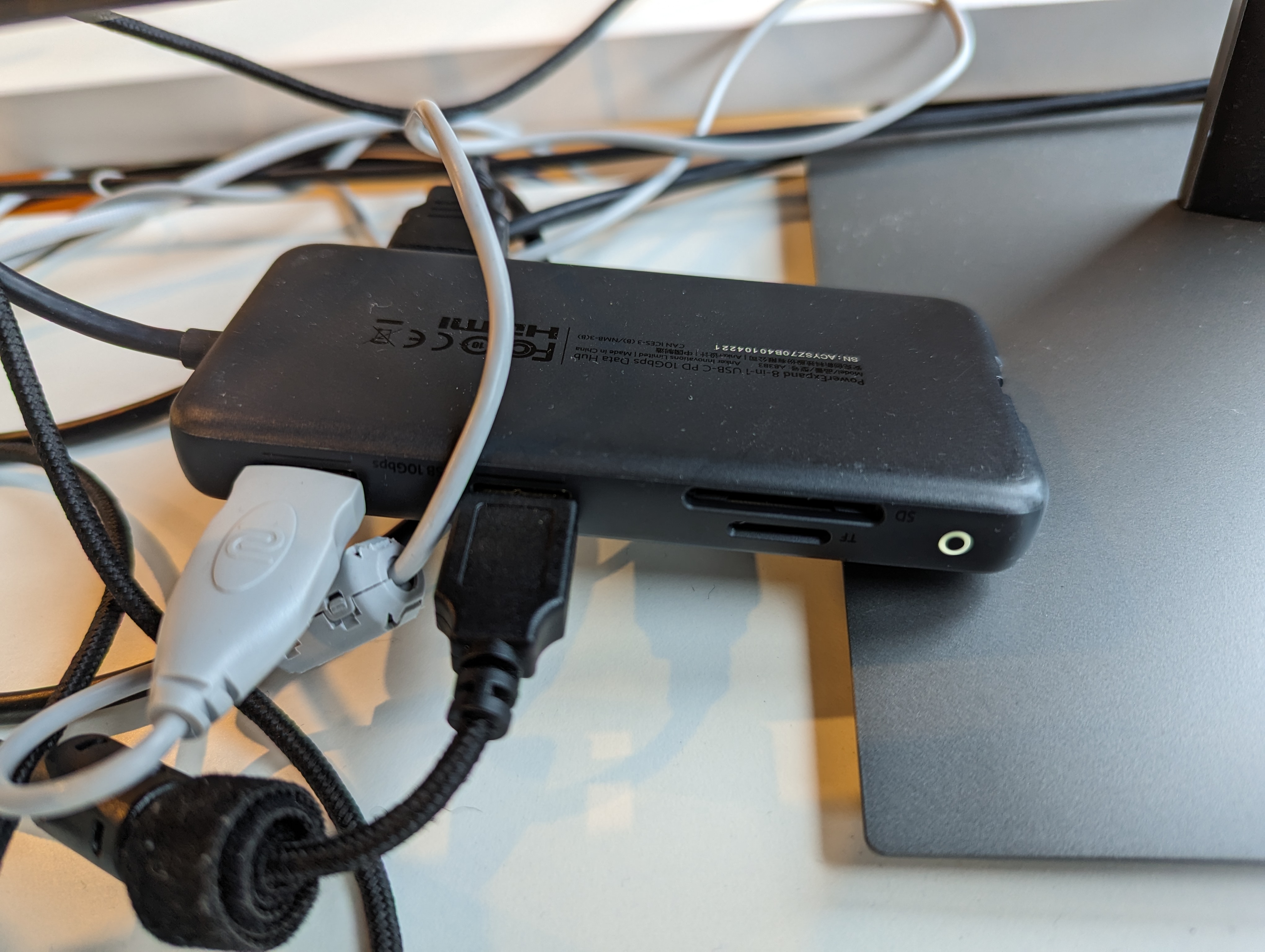 A photograph of an Anker USB hub with two USB-A cables plugged into it in the front as well as an HDMI cable plugged into it in the back.  It has a circular white light on the front right which is illuminated.